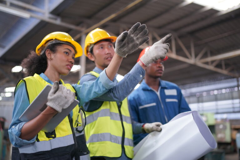 Male and Female Industrial Engineers Talk with Factory Worker against machines and equipments background. They Work at the Heavy Industry Manufacturing Facility